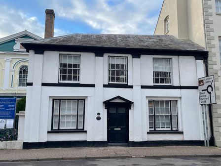 A two-story white house with black window frames and a black door next to a road sign at The Hame in Monmouth