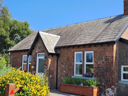 Exterior view of a stone cottage with a slate roof yellow flowers and planters near the entrance at Bogrie Cottage in Canonbie near Gretna Green