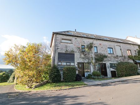 A stone building with multiple windows and doors surrounded by bushes and trees at Magnolia House in Dittisham