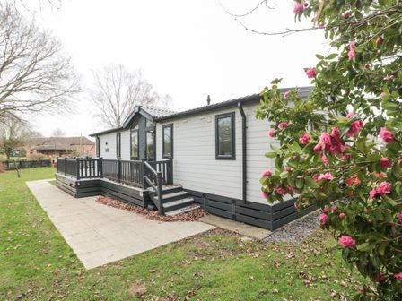 A white and gray prefab house with a small porch and steps surrounded by grass and pink flowers at Owls Nest in Furzehill