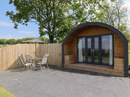 An outdoor patio area with a table and four chairs under an umbrella next to a curved wooden cabin at Dryfe Lodge in Lockerbie