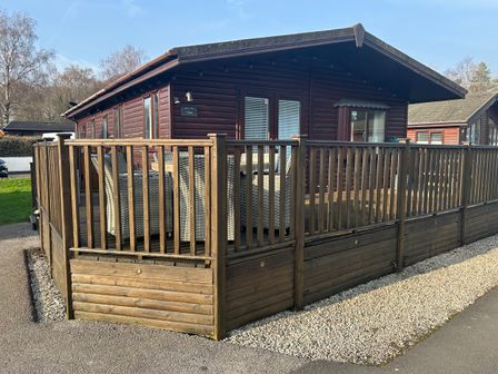A wooden cabin with a deck and fence at Lake View Lodge, Lakeside 3, White Cross Bay, Windermere