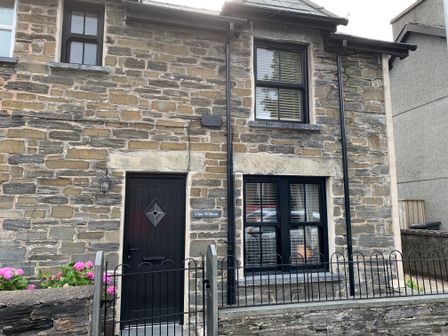 The front exterior of a stone house with black windows and a black door at Glan William in Dolwyddelan