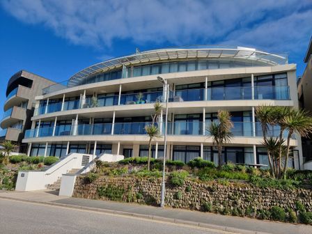A modern three-story building with glass balconies and landscaped garden in front at Fistral Pearl in Newquay