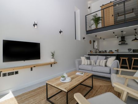 A modern living room with a wall-mounted TV a gray sofa a wooden coffee table and an open kitchen at Basswood Barn in Lime Tree Barn