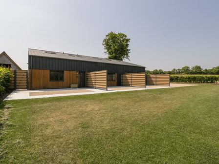 A modern house with wooden fencing and a large grass lawn at Linden Barn in Wincanton