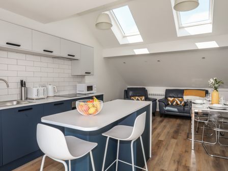 A kitchen with island and stools next to a living area with sofas and a dining table at Golygfa'r Gastell Castle View in Criccieth