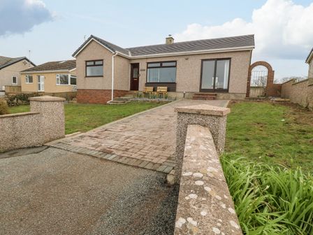 A single-story house with a paved driveway and green lawn at Awelfryn in Llanfaelog near Rhosneigr
