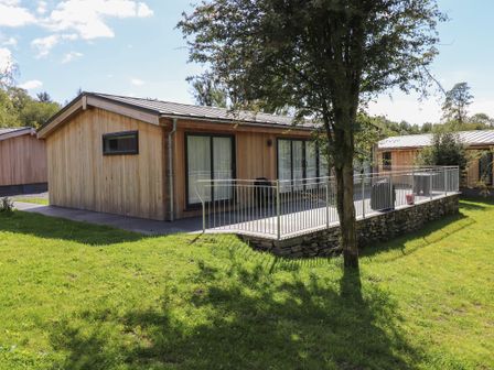 A wooden cabin with a metal roof and a patio area surrounded by a railing on grass at Hawthorn Croft in Haverthwaite