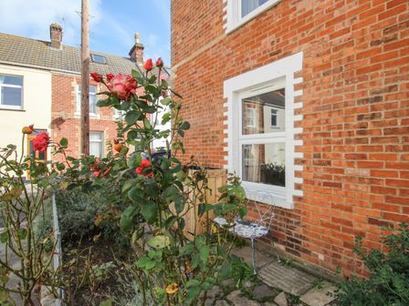 A garden with red roses and a metal chair beside a brick house at The Corner House in Weymouth