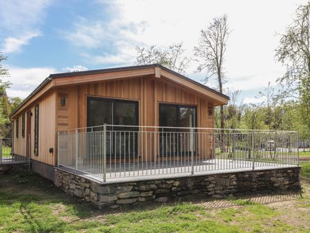 A wooden house with a stone foundation and metal railing around a patio at Blackthorn Copse in Haverthwaite