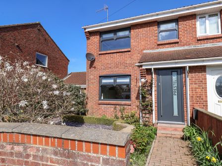The front exterior of a brick semi detached house with a garden and a path leading to a dark grey door at Prestella in Filey