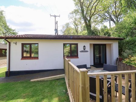 A small single-story building with two windows wooden deck with outdoor table and chairs at Larchwood Lodge in Combe Martin