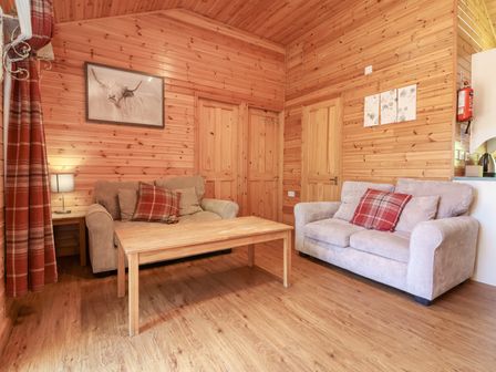 A living room with two sofas a wooden coffee table wooden walls and doors and red plaid cushions at Chalet Lodge Bunks L1 in Combe Martin