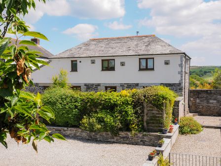 A stone and white two-story house with shrubs and potted plants in a gravel courtyard at Great Brightor Cob Barn in St Kew Highway