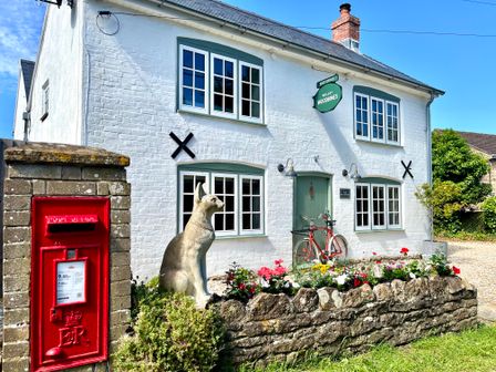 A white brick building with green framed windows a red post box a stone statue of a dog a garden with flowers and a red bicycle at Old Post Office Sherborne