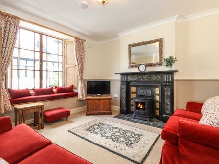 A living room with a fireplace a large window with cushions a television and red sofas at Primrose Cottage Keswick