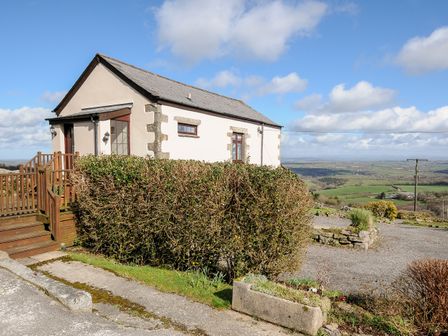 An exterior view of a small house with hedge and wooden stairs overlooking fields at Cheesewring Cottage Minions near Upton Cross