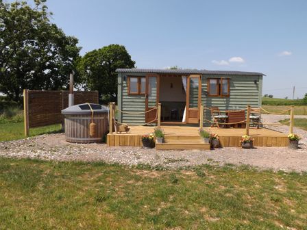An outdoor wooden deck with a seating area and hot tub outside a small green cabin at Tawny in Morchard Bishop