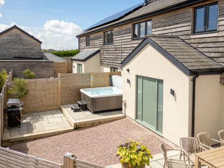 A backyard with a hot tub grill dining table and chairs at Farmyard House in Llanfechell