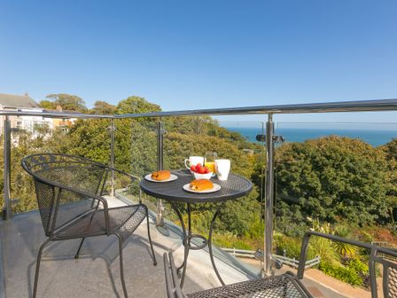 A balcony with a black metal table and chairs overlooking trees and the sea at Bay View in Carbis Bay