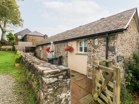 An exterior view of a stone cottage with a wooden gate and outdoor seating at Cosy Cottage in Broadwoodwidger near Lifton