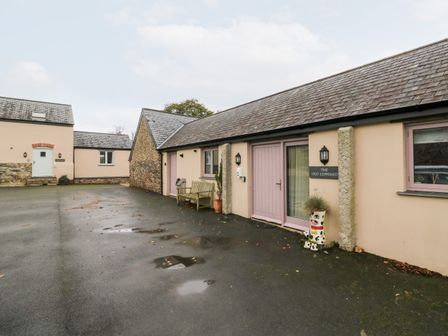 An exterior view of a building with a bench and decorative planter outside at The Old Cowshed Broadwoodwidger near Lifton