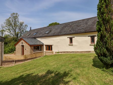An exterior view of a barn style building with grass and trees at Bunts Barn Northlew near Hatherleigh