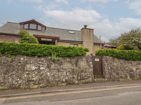 A house with a stone wall and green hedge with a wooden gate at Spernenwyn in St Ives