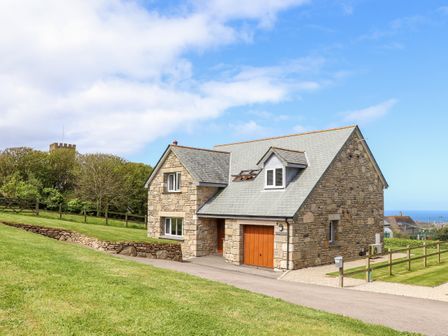 A stone house with a sloped roof and wooden garage door on a grassy hill at Charlottes House in Pendeen