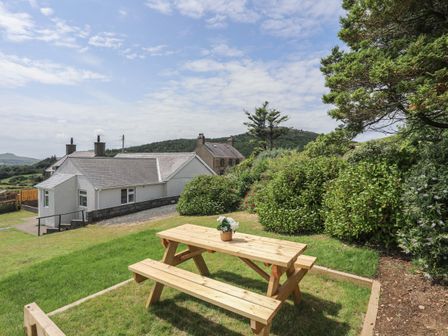 A wooden picnic table with a flower pot on grass with houses and trees in the background at Glan Awel in Nefyn
