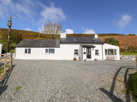 A white cottage with a gravel driveway and hills in the background at Pennant Cottage in Llithfaen