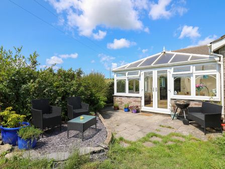 An outdoor patio with black wicker chairs a glass table potted plants and a conservatory at Ty Cariad in Llangynin near St Clears