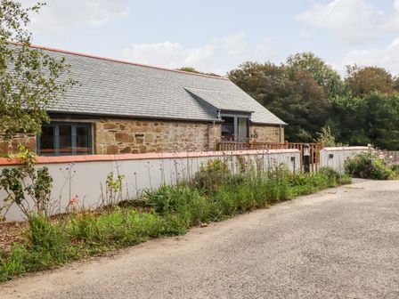A stone building with a slate roof behind a white wall with flowers and plants at Carines Barns - Pol in Cubert