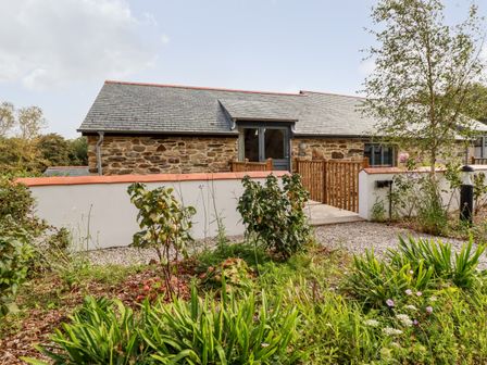 A stone building with a slate roof behind a wooden gate and garden at Carines Barns - Par in Cubert