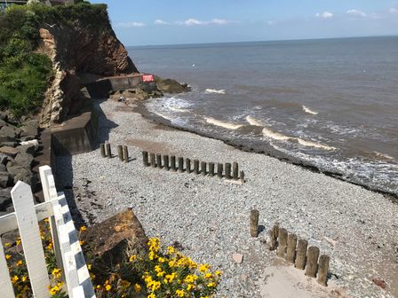 A rocky beach with wooden posts near the water and a cliffside with a warning sign at Oyster Catchers in Watchet