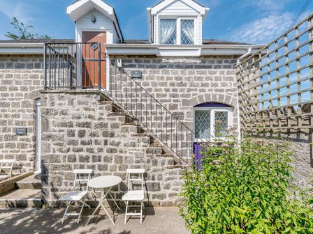 Stone building exterior with metal staircase white chairs and table and greenery at The Hayloft in St Florence