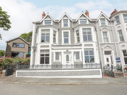 A grey and white three-story house with bay windows and a small front garden with a black metal fence at Llwyn Onn in Criccieth