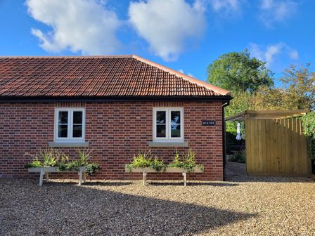 A brick building with two white windows and two flower planters outside at Beck View Weston Longville near Lenwade