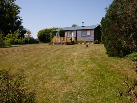 A small house with a wooden deck in a large garden with trees and bushes at Y Caban Glas in Rhydlewis near Brynhoffnant