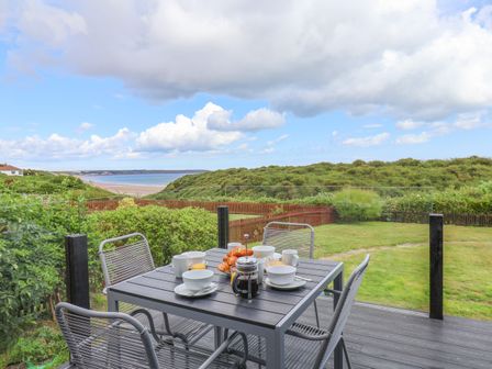 An outdoor patio with a table set for breakfast overlooking green bushes and a beach at 29 Gap Road in Hunmanby
