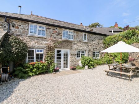 A stone cottage with white framed windows plants and a picnic table with umbrella in a gravel yard at Henwood Barn Henwood near Upton Cross