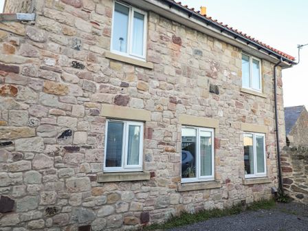 Stone exterior wall of a house with six white framed windows at 30 Union Street in Seahouses