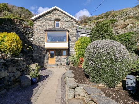 Stone house with wooden door and large window front garden with path shrubs and stone walls at Ty'n-Y-Ffynnon Cottage in Barmouth
