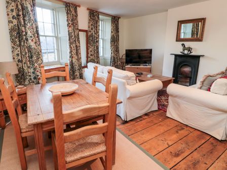 A living room with wooden dining table and chairs white sofas fireplace and television at Upper Oakwood in Alnwick