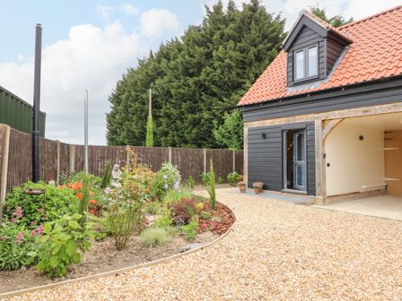 A gravel driveway with flower beds next to a black wooden house with a red tiled roof at Strawberry Fields Annex in Emneth