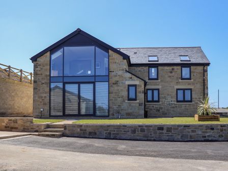 A stone house with large windows and a small garden area at The Waves in Amble