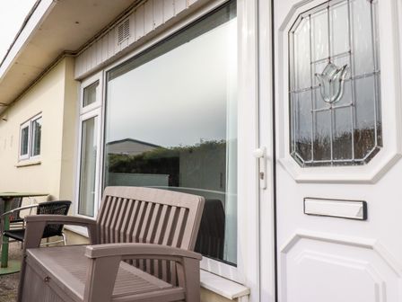 The exterior of a building with a white door featuring decorative glass a large window a brown bench and a small table with chairs at Sandpiper in Perranporth