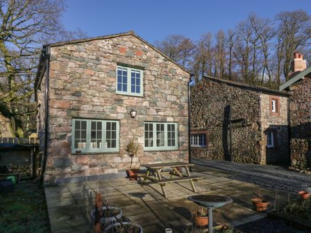 A stone house with green windows and a wooden picnic table on a paved patio at The Barn in Nether Wasdale