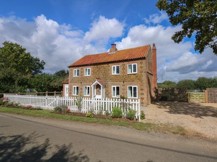 A stone cottage with a tiled roof and white picket fence along the roadside at Horseshoe Cottage in Pentney